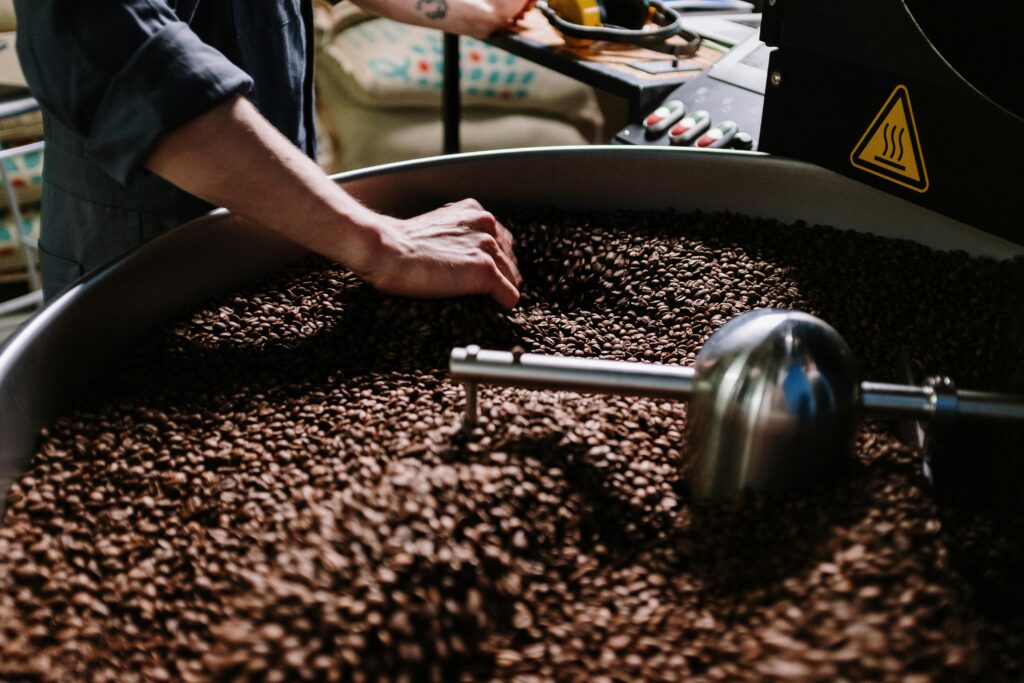 Close-up of hand inspecting roasted coffee beans in a commercial roaster drum, highlighting food industry processing equipment oil free air